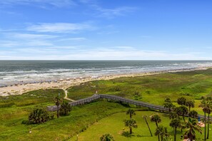A coastal view with a wooden boardwalk leading to a beach area. - Galvestonian by Ryson Vacation Rentals (Galveston)