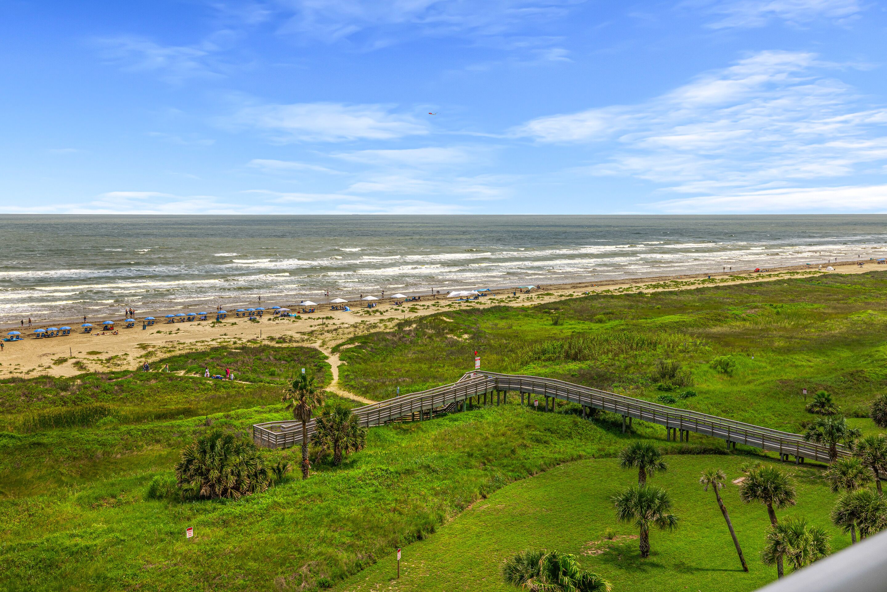 A coastal landscape with a beach, a wooden boardwalk, and a bridge over water.