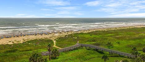 A coastal landscape with a beach, a wooden boardwalk, and a bridge over water.