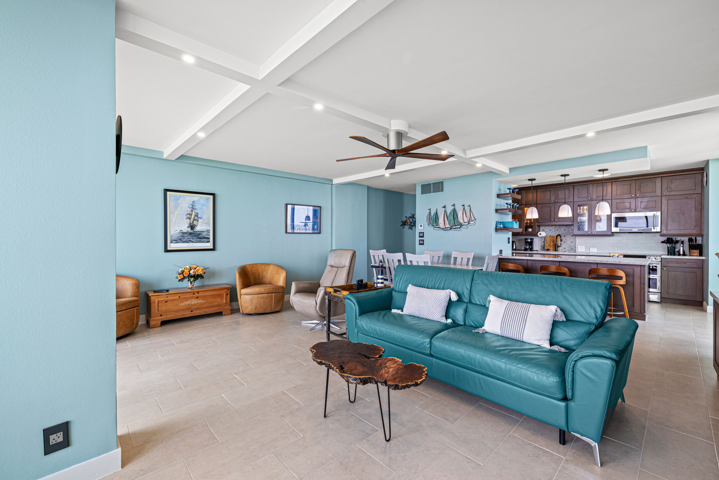 A spacious living room with a teal sofa, a wooden coffee table, and a ceiling fan.