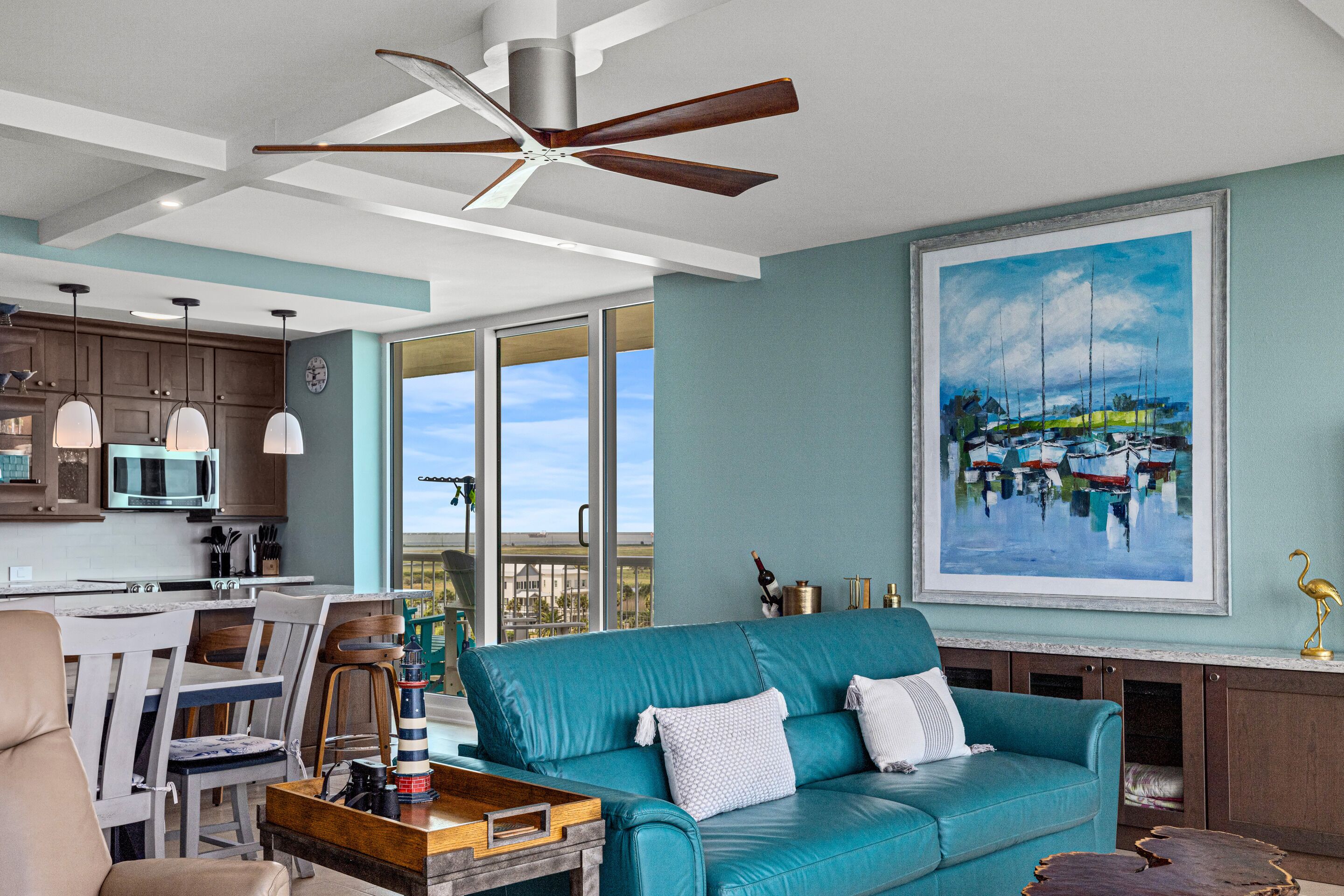 A modern living room with a teal sofa, a wooden coffee table, and a painting of boats on the wall.