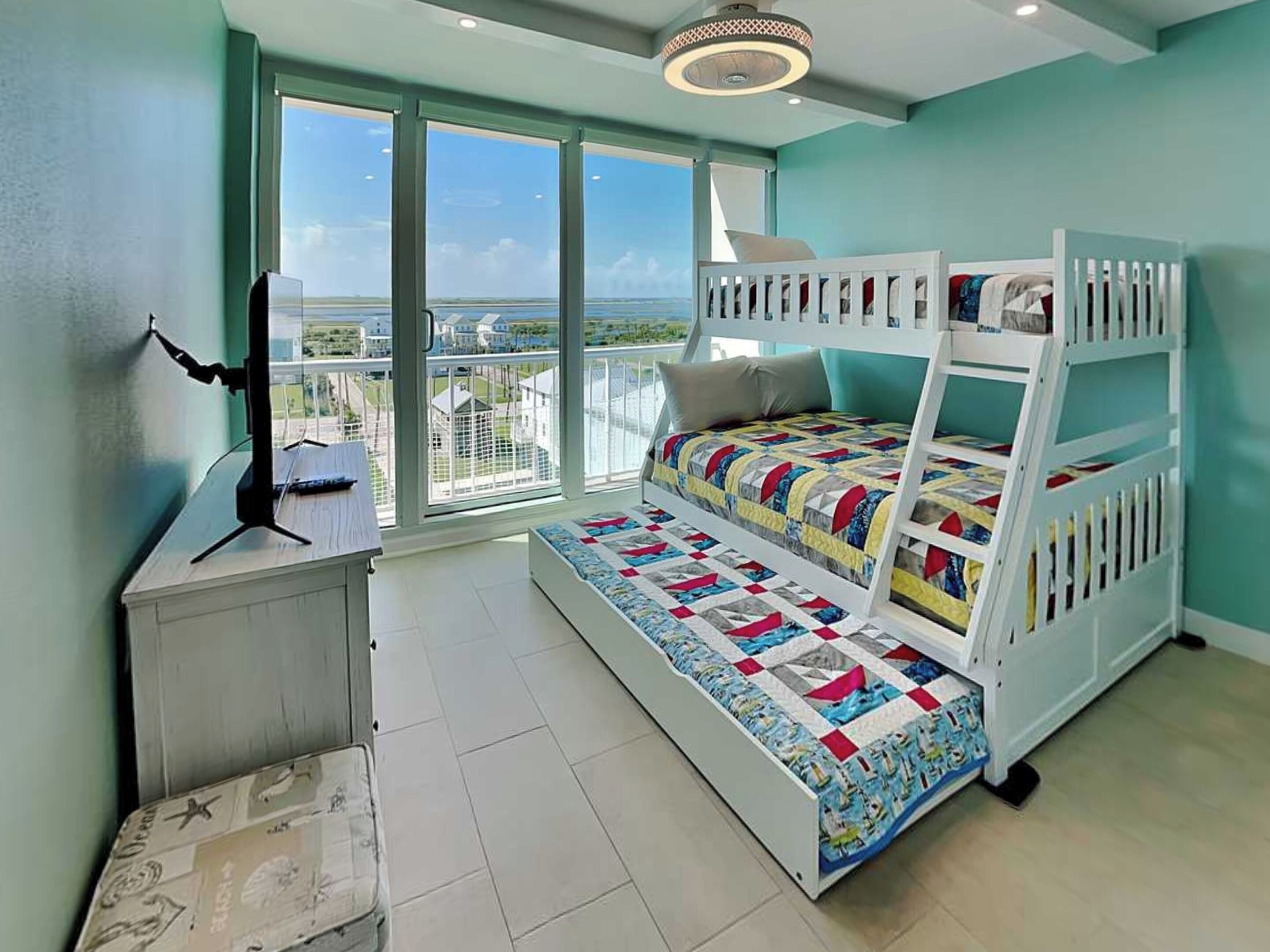 Une chambre avec un lit superposé, de grandes fenêtres, un bureau et une vue sur la mer.