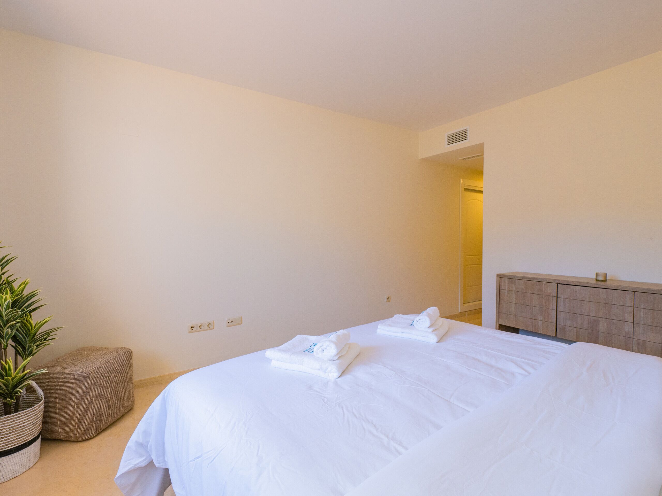 Una habitación de hotel con una cama grande, una mesita de noche, una planta en maceta y un cabecero de madera.