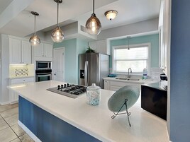 Una cocina moderna con armarios blancos, un refrigerador de acero inoxidable, una estufa a gas e iluminación colgante.
