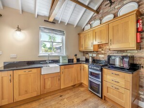A kitchen with wooden cabinets, a sink, a stove, a microwave, and a window with a view of the outside.