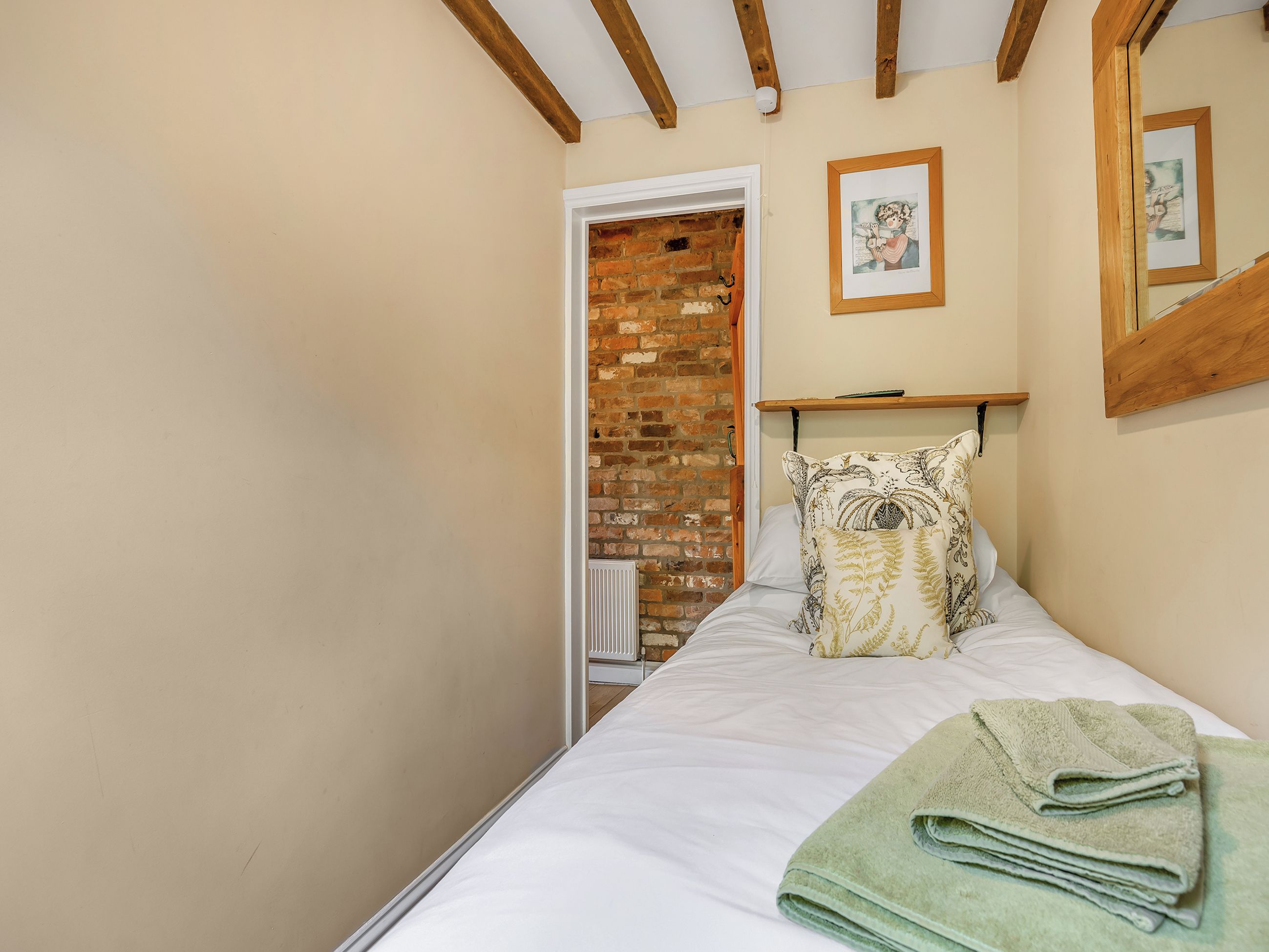 Ein Schlafzimmer mit Backsteinwand, einem Bett mit weißer Bettwäsche, einem grünen Handtuch und einem gerahmten Bild an der Wand.