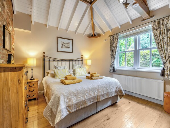 A bedroom with a bed, bedside lamps, a wooden dresser, a window with curtains, and a radiator.