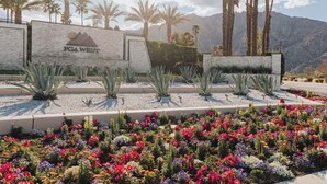 A landscaped area with a sign reading "PGA WEST" surrounded by palm trees and a variety of colorful flowers. - End of Summer Golf Getaway | PGA West | Golf Cart (La Quinta)