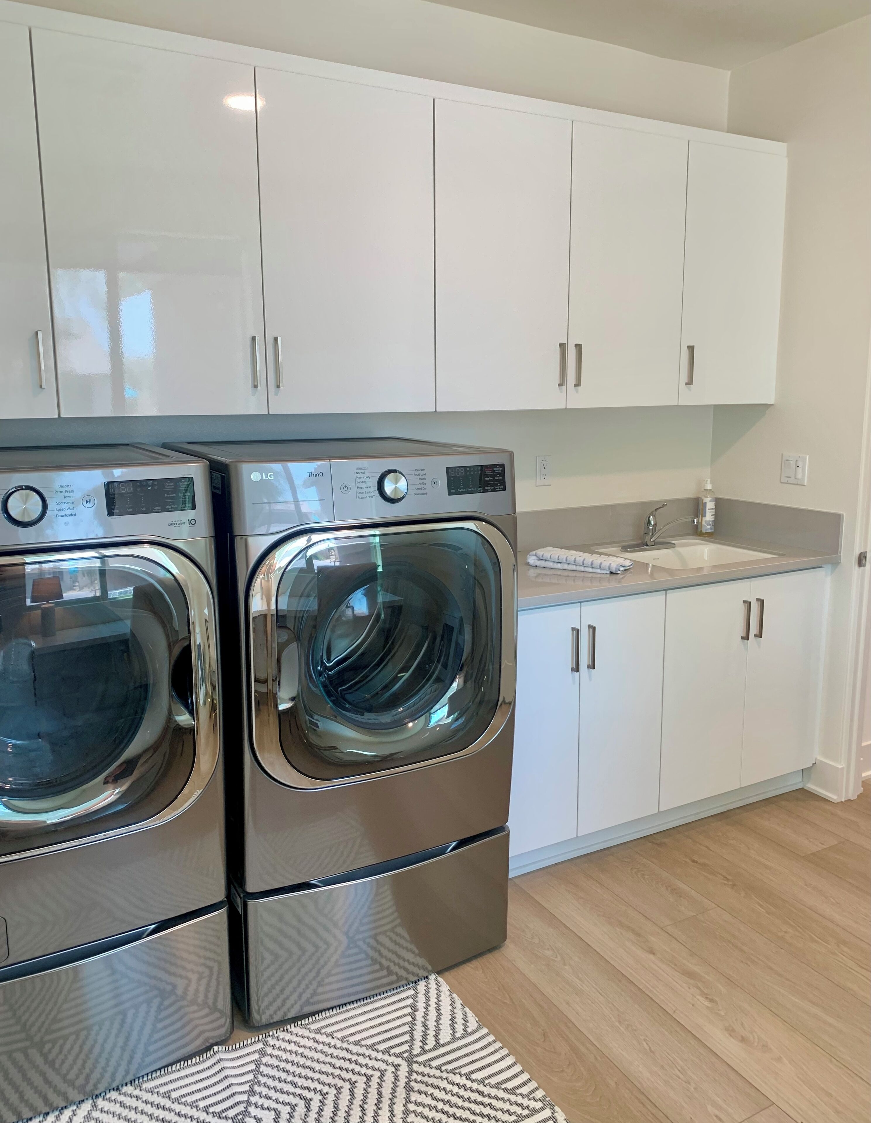 A modern kitchen with stainless steel appliances, white cabinets, and a wooden floor.