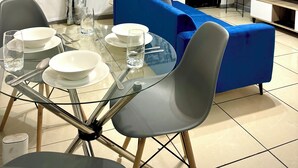 Un salon moderne avec un canapé bleu, une table à manger en verre pour quatre personnes et un téléviseur posé sur un meuble.