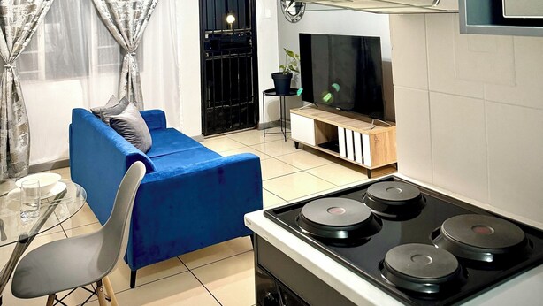 Un espace de vie compact comprenant un coin cuisine, un canapé bleu, une table à manger avec des chaises et un téléviseur.