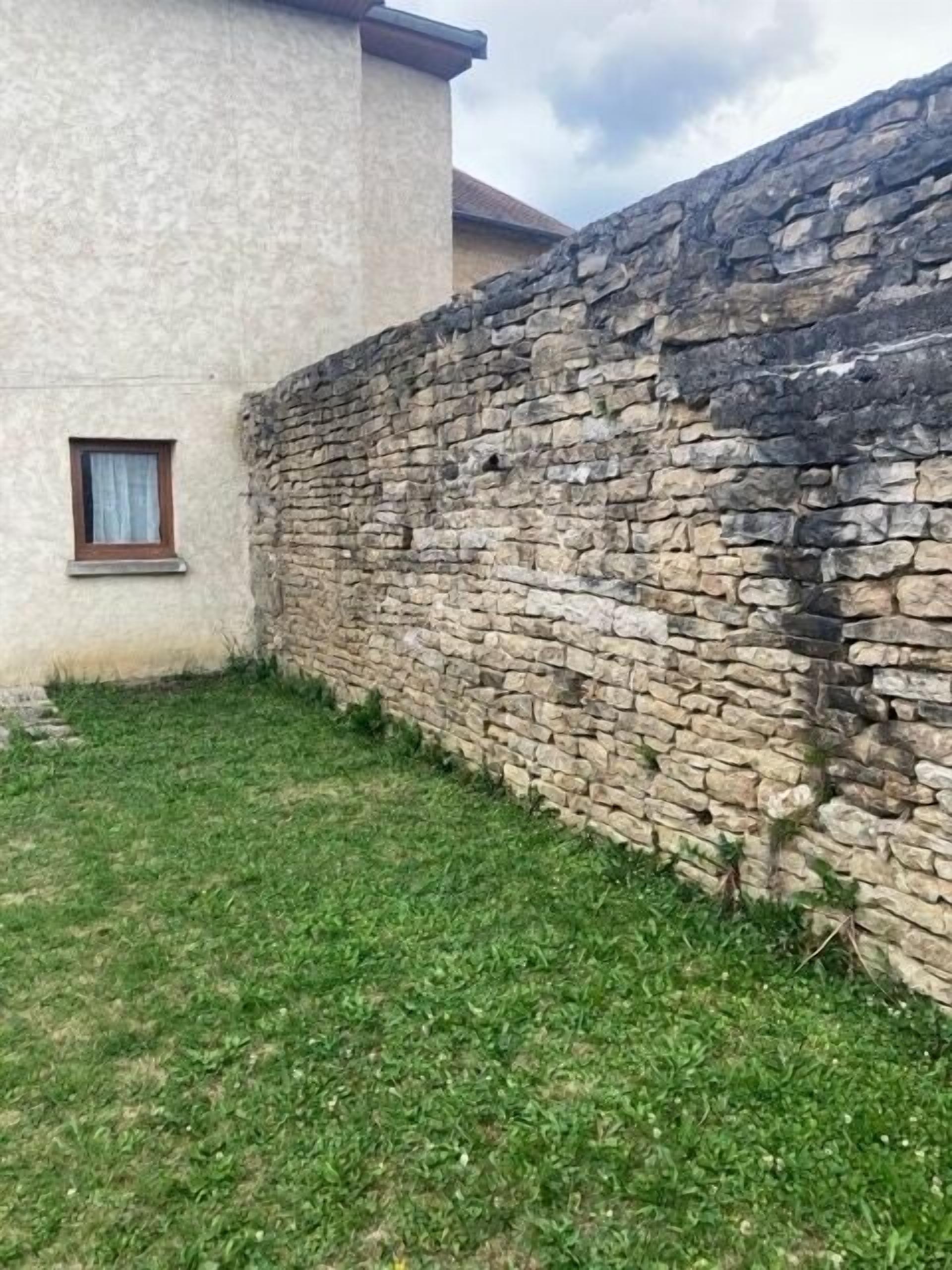 A stone wall adjacent to a building with a small window.