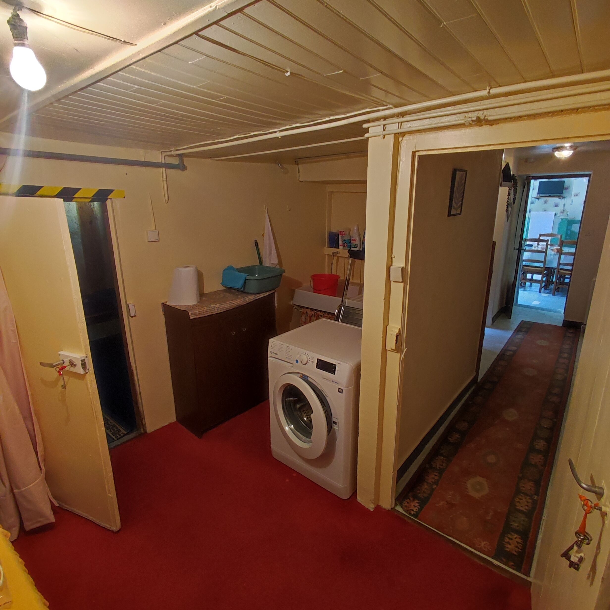 A compact laundry room with a washing machine, a small table with cleaning supplies, and a red carpeted floor.