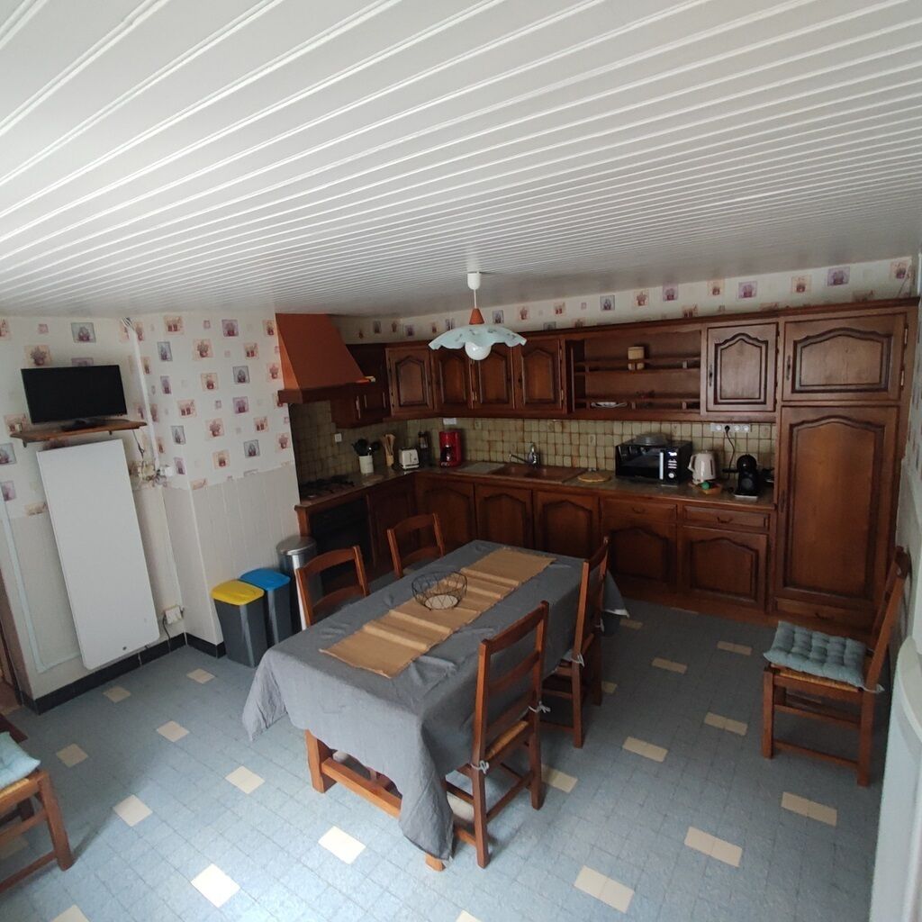 A compact kitchen with wooden cabinets, a dining table with chairs, and a TV on a stand.