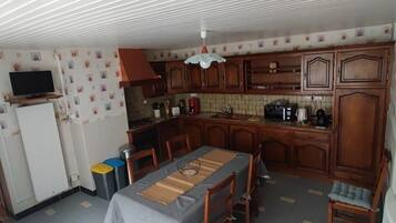 A compact kitchen with wooden cabinets, a dining table with chairs, and a TV on a stand.