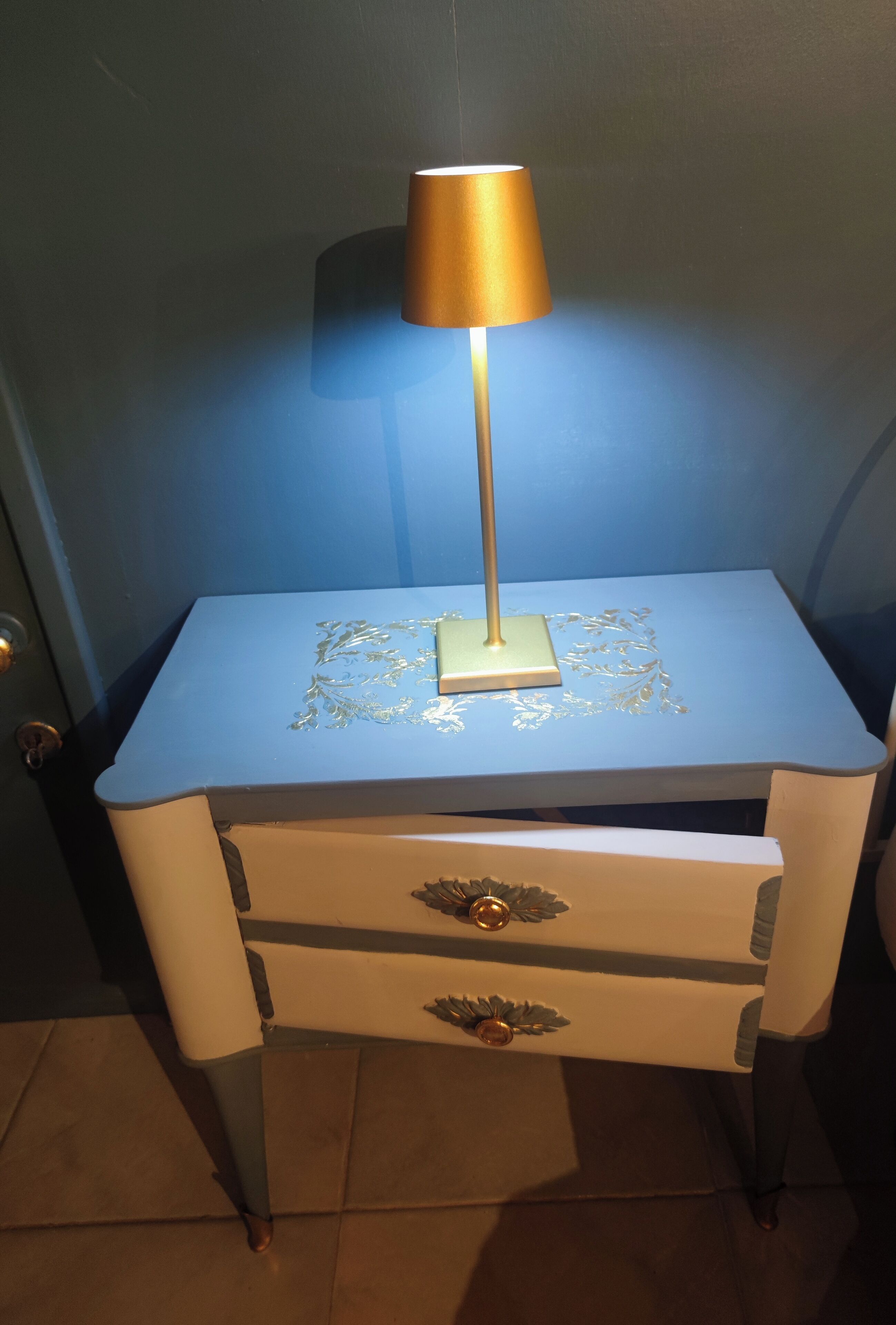 A bedside table with a lamp, a drawer, and a decorative pattern on the tabletop.