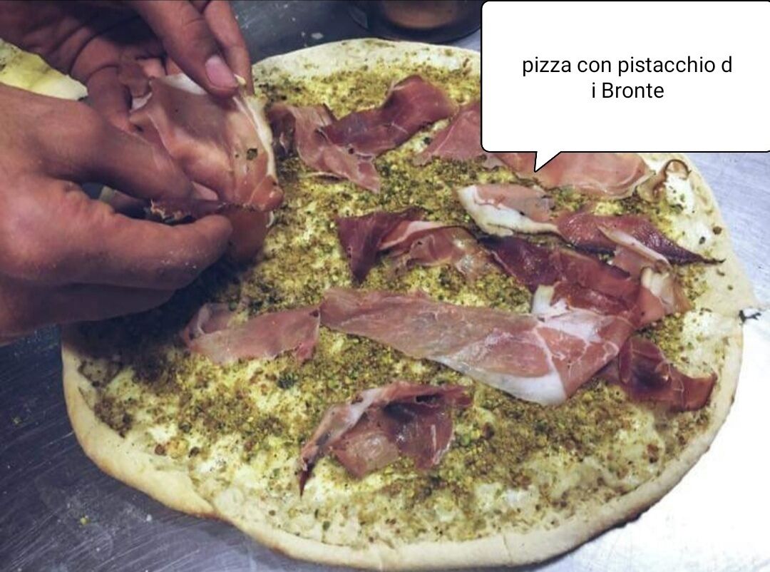 Une pizza en cours de préparation, garnie de pesto et de jambon de Parme.