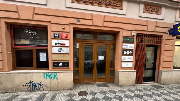 Un edificio con entrada de baldosas, carteles de diversos comercios y una puerta con reja de metal.