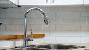 Eine Küche mit Spülbecken aus Edelstahl, einem modernen Wasserhahn und einer weißen Fliesenwand.