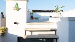Una escalera exterior moderna que conduce a una terraza en la azotea, con una pared blanca, una planta verde y una pequeña mesa.
