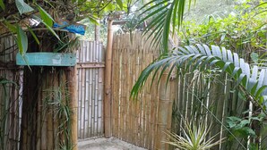 Una cerca de bambú con un pequeño portón, rodeada de abundante vegetación y plantas colgantes.