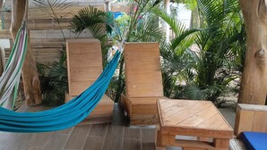 Una terraza de madera con una hamaca, bancos de madera y plantas en macetas.