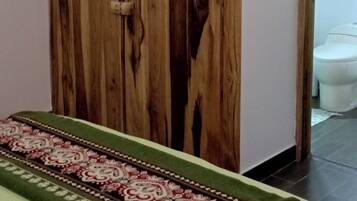 A room with a wooden wardrobe, a bed with a patterned bedspread, and a toilet visible through an open doorway.