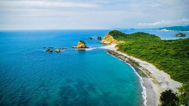 Un paisaje costero con playa, afloramientos rocosos y abundante vegetación.