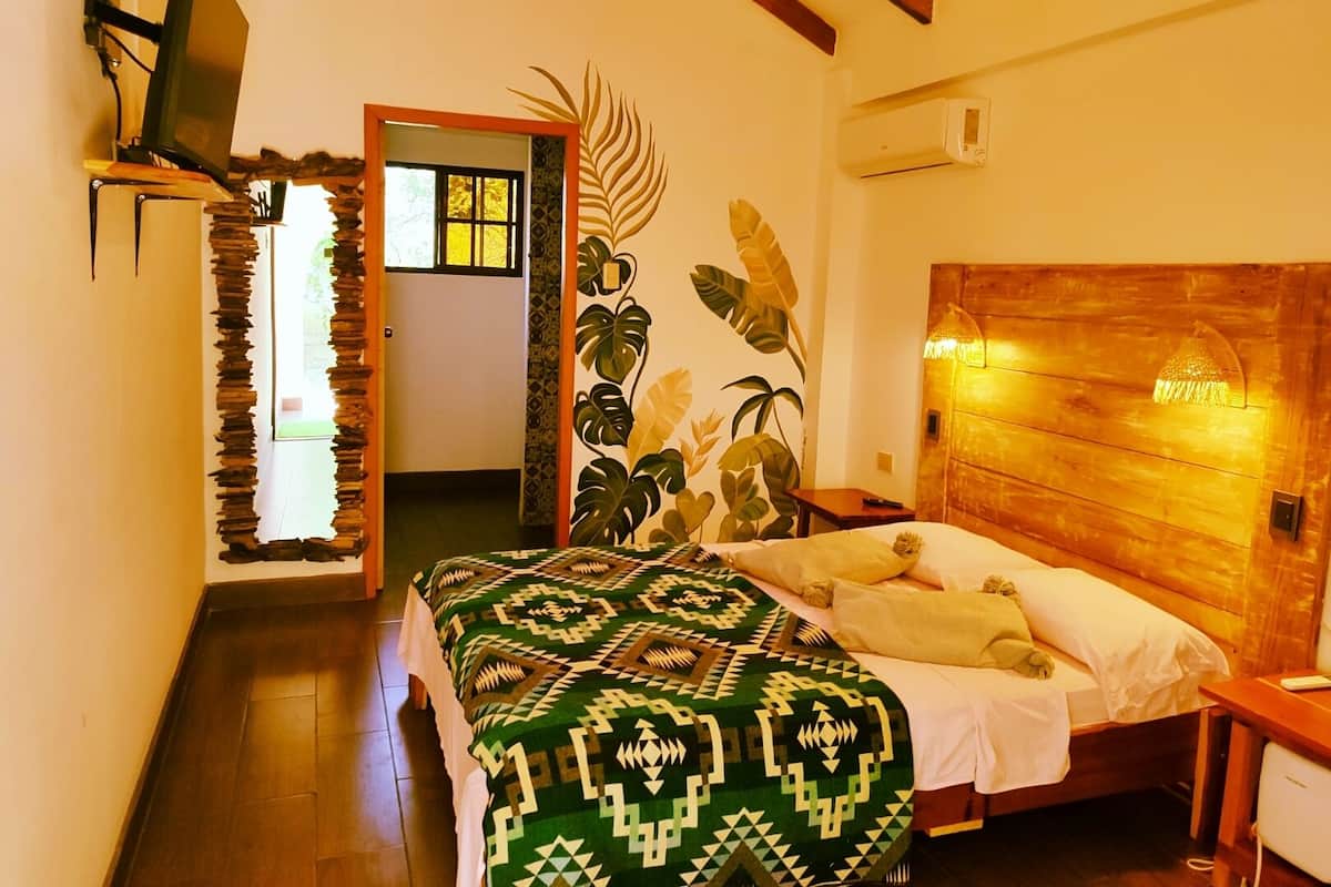 A room with a bed, a wooden headboard, a wall-mounted TV, and a door leading to another room.