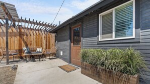 Une terrasse en bois avec des chaises, un jardinier en bois contenant des plantes, et une maison à l’extérieur sombre et aux encadrements de fenêtres blancs.