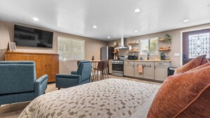 Un salon moderne avec un grand lit, deux fauteuils bleus, un meuble en bois et un téléviseur.