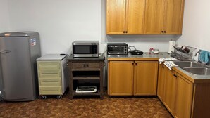 A compact kitchen with wooden cabinets, a stainless steel refrigerator, a microwave, a toaster oven, and a small countertop with a sink. - Cozy 2-bedroom apartment with WiFi, AC in amazing Penticton (Penticton)