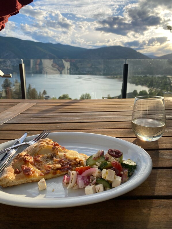 A meal on a wooden table with a glass of water, overlooking a lake and mountains.