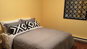 A bedroom with a bed, pillows, a nightstand, a wall-mounted artwork, and a carpeted floor. - Cozy 2-bedroom apartment with WiFi, AC in amazing Penticton (Penticton)