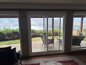 A room with a view of a lake and mountains through large sliding glass doors.