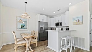A modern kitchen with white cabinetry, a stainless steel refrigerator, a microwave, and a small island with stools. - Waterfront 2BR Condo *Renovated 2025*  Marina Pool (Orange Beach)
