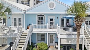 A light blue two-story house with white railings, a front porch, and a palm tree. - Waterfront 2BR Condo *Renovated 2025*  Marina Pool (Orange Beach)