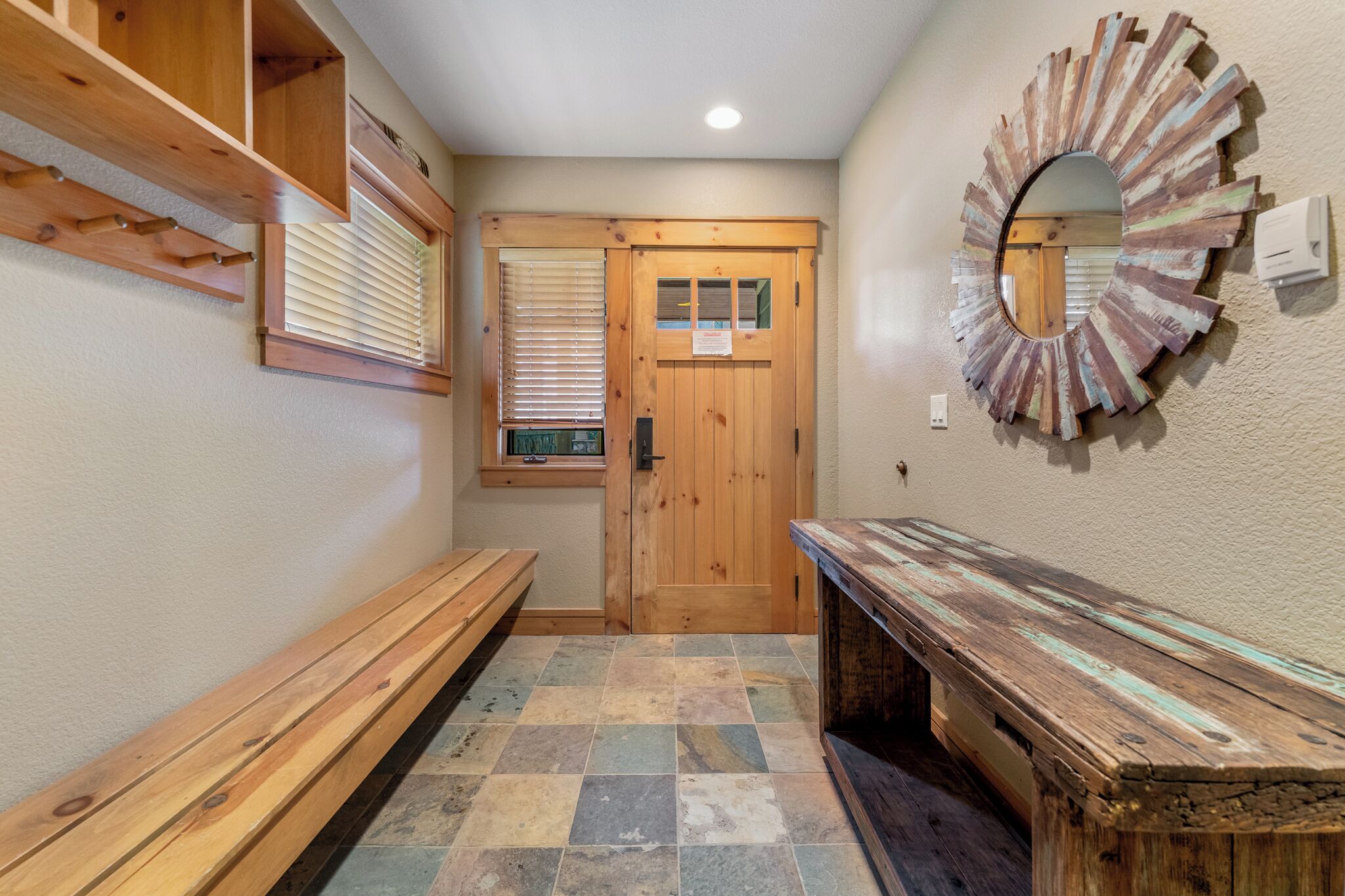 A hallway with wooden benches, a wooden door, and a mirror on the wall.