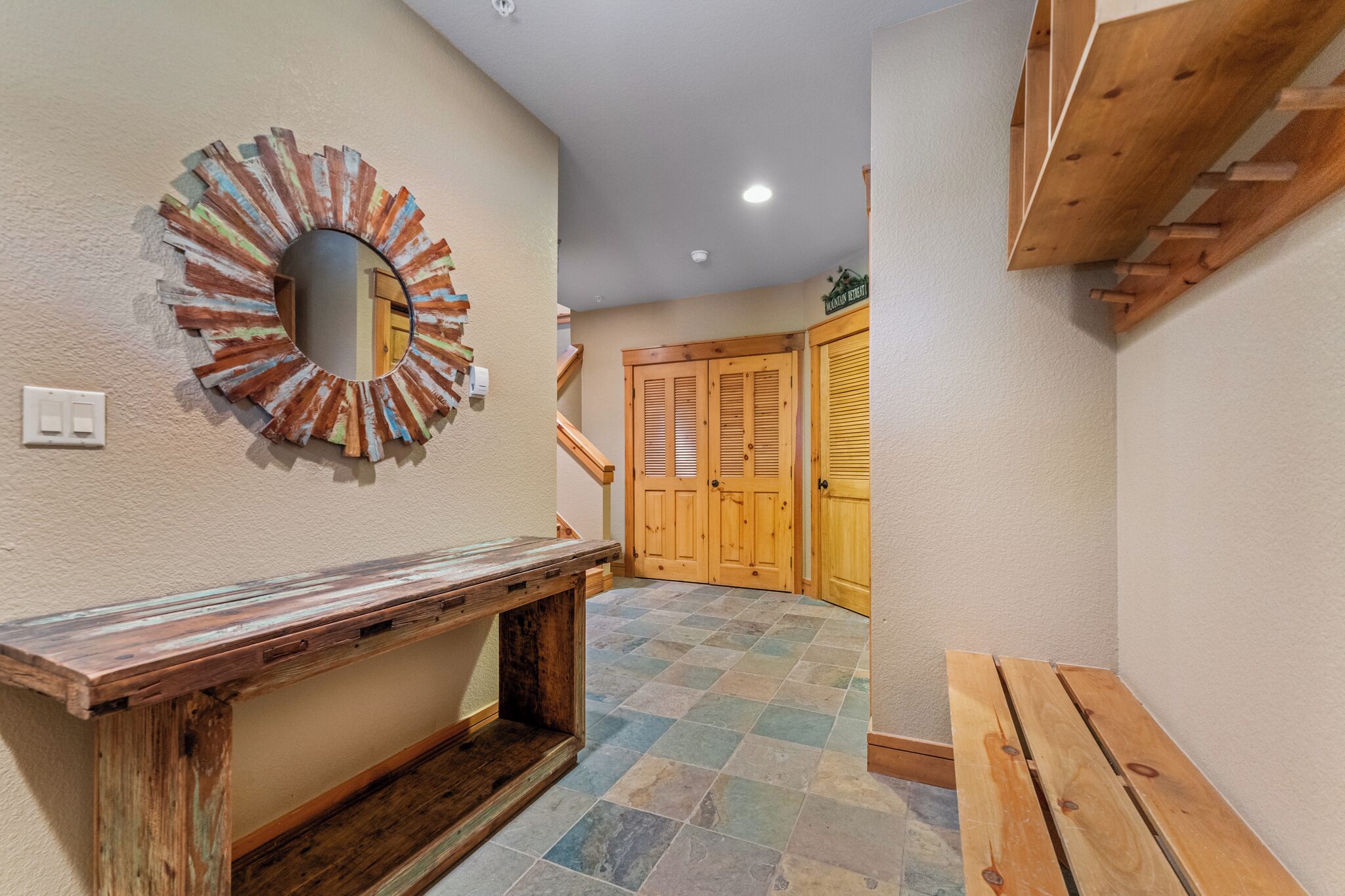 A hallway with a rustic wooden bench, a mirror with a sunburst design, and a wooden door with a sign above it.