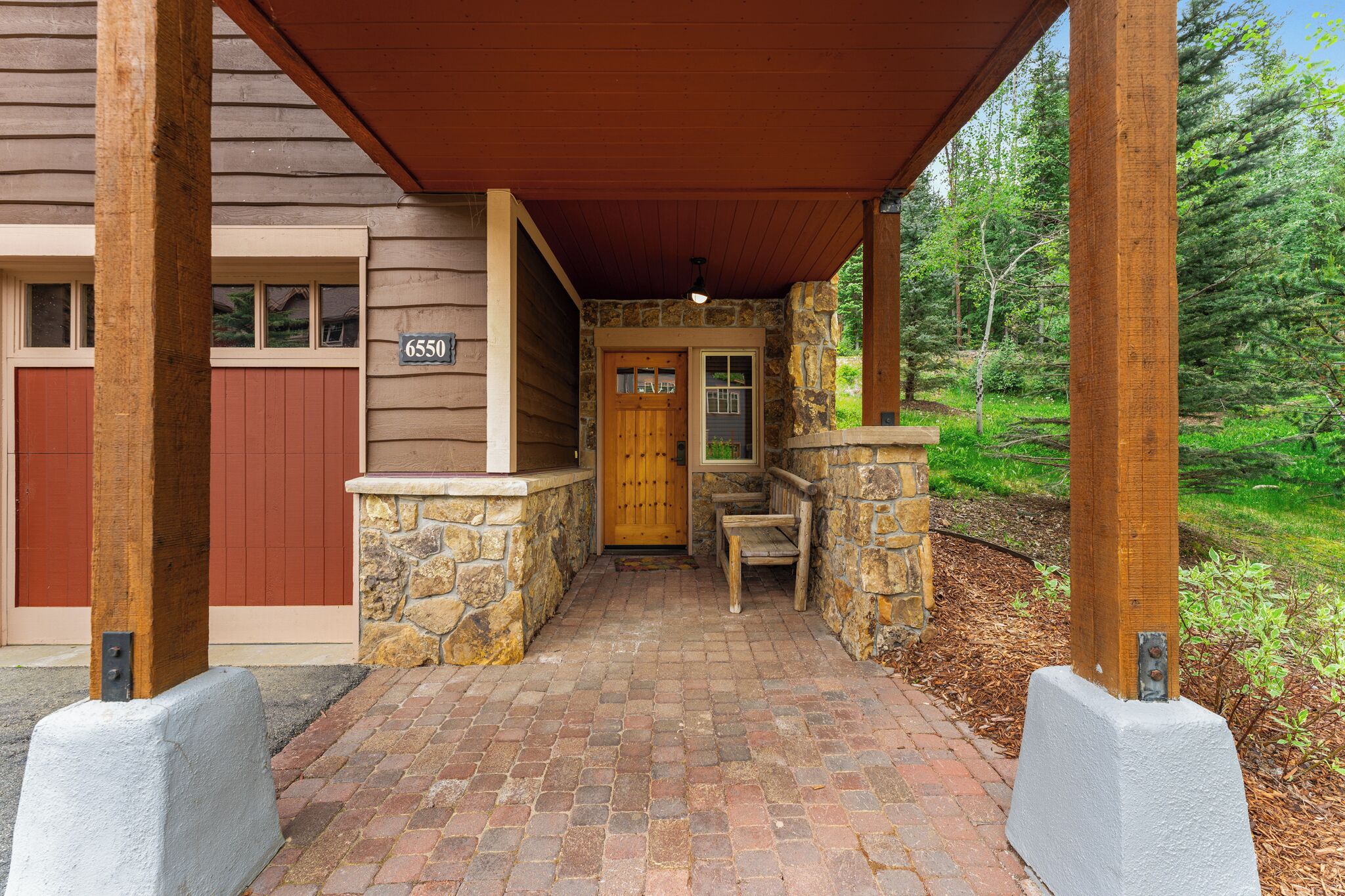 A covered porch with a stone wall, a wooden door, and a bench.