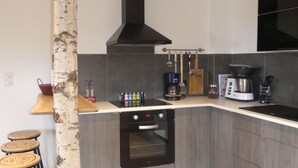 A modern kitchen with a built-in oven, a coffee maker, and a birch tree trunk as a decorative column. - LE Massif - Appartement Avec vue Imprenable (La Bresse)
