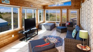 A spacious living room with a large TV, comfortable seating, and large windows offering views of the outdoors. - Back Bay Dog- Pool, Hot Tub, Bay, Sleeps 13 (Virginia Beach)