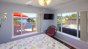 A bedroom with a large bed, a chair, a TV, and a balcony with a hot tub and outdoor furniture. - Back Bay Dog- Pool, Hot Tub, Bay, Sleeps 13 (Virginia Beach)