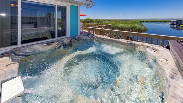 A hot tub on a deck with a view of a body of water and a building with glass doors. - Back Bay Dog- Pool, Hot Tub, Bay, Sleeps 13 (Virginia Beach)