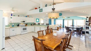 A spacious kitchen with white cabinets, a wooden dining table, and a ceiling fan. - Back Bay Dog- Pool, Hot Tub, Bay, Sleeps 13 (Virginia Beach)