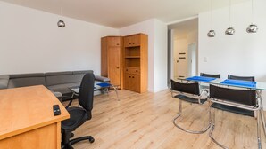 A modern, well-lit room with a wooden desk, a grey sofa, and a dining area with metal chairs. - Molo Centrum by Grand Apartments (Sopot)