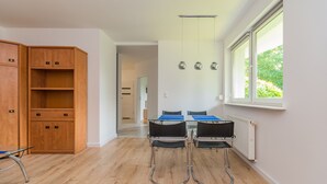 A room with a wooden cabinet, a table with chairs, and a window with a view of greenery. - Molo Centrum by Grand Apartments (Sopot)