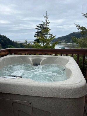 A hot tub on a deck with a view of a lake, trees, and a bridge in the background. - The Hideaway Cabin #63 (Gold Beach)