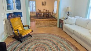 Un salon avec un fauteuil jaune, un canapé blanc, une table à manger avec des chaises et un tapis à motifs.