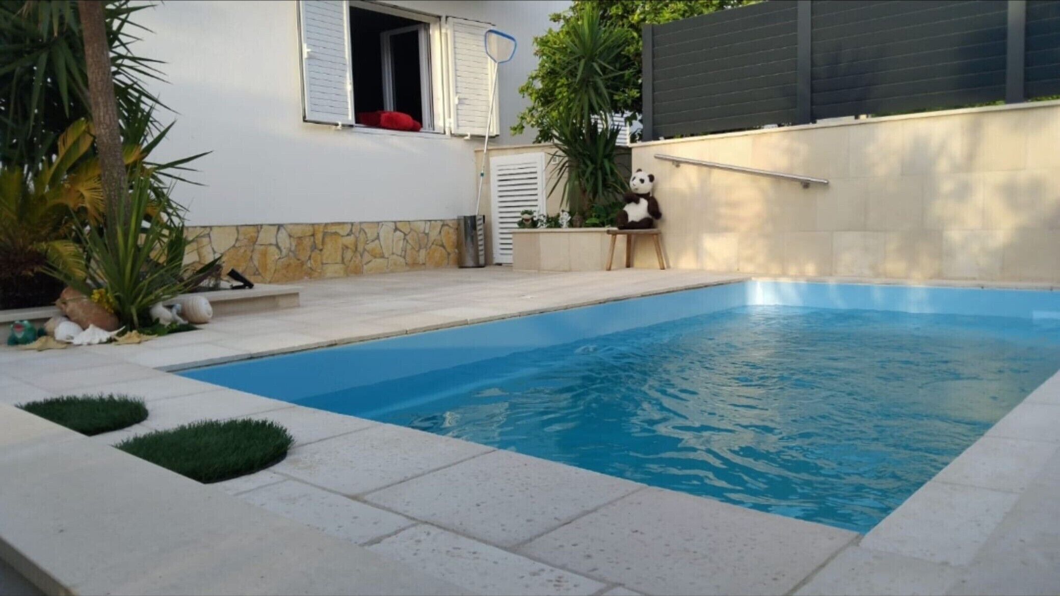 Une piscine avec un mur en pierre et un petit espace aménagé en jardin.